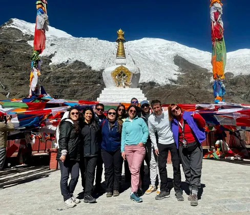 Un viaggio di gruppo WeRoad posa per una foto davanti a uno stupa bianco con un ghiacciaio e montagne innevate sullo sfondo.