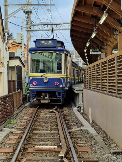 Un treno d'epoca blu e crema fermato in una stazione con una banchina di legno, visto frontalmente lungo i binari.