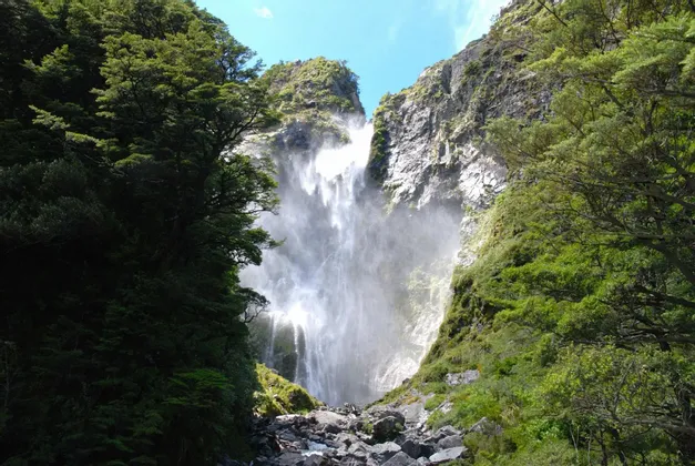 Ein gewaltiger Wasserfall stürzt eine felsige Klippe hinab, umrahmt von üppiger grüner Vegetation in einer steilen Schlucht.