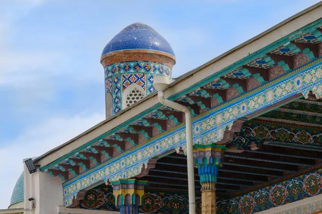 Un primo piano di un edificio ornato con una cupola piastrellata di blu e grondaie riccamente decorate, contro un cielo azzurro.