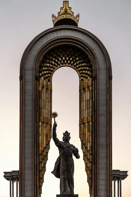 Una statua di bronzo di un re incoronato che alza uno scettro, incorniciata in un grande arco sontuoso sormontato da una corona.