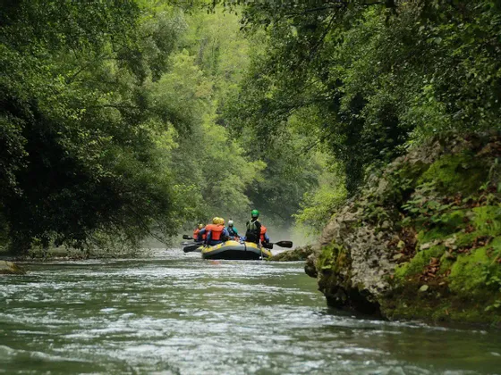 Un viaggio di gruppo WeRoad fa rafting su un gommone lungo un fiume circondato da una fitta foresta verde.