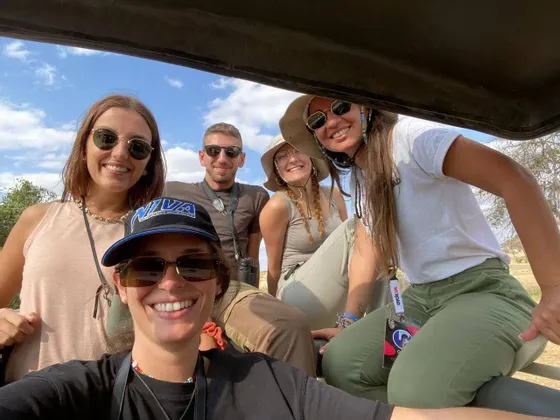 Un voyage de groupe WeRoad souriant pour un selfie à l'intérieur d'un véhicule de safari sous un ciel ensoleillé.