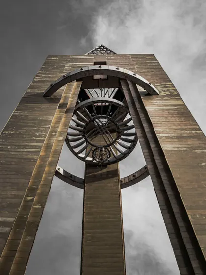 Una ripresa dal basso di un'alta torre di cemento con una grande sfera armillare metallica sospesa contro un cielo coperto.