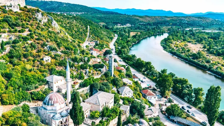 Eine Luftaufnahme einer historischen Stadt mit einer Moschee und einem Uhrturm, gebaut auf einem grünen Hügel neben einem gewundenen Fluss.