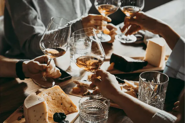 Un grupo de WeRoad brindando con copas de vino sobre una mesa de madera con quesos variados.