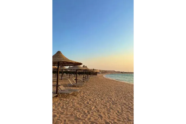 Una fila di lettini vuoti e ombrelloni di paglia fiancheggia una spiaggia sabbiosa in riva al mare al tramonto.