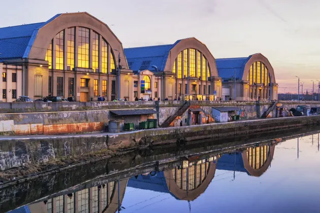 Tre grandi edifici ad arco con finestre dorate e luminose, riflesse in un canale al tramonto.