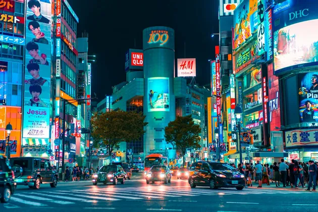 Un vivace incrocio cittadino di notte, con traffico intenso e alti edifici illuminati da colorati cartelloni al neon.