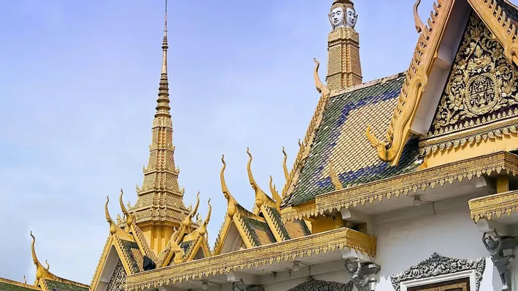 Les flèches dorées ouvragées et les toits de tuiles d'un temple traditionnel d'Asie du Sud-Est sous un ciel bleu clair.