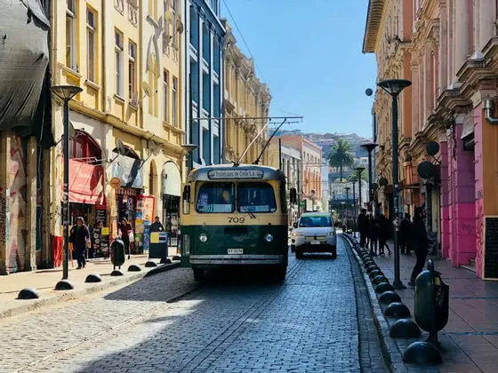 Un filobus d'epoca verde e giallo percorre una stretta strada acciottolata tra edifici colorati in una giornata di sole.