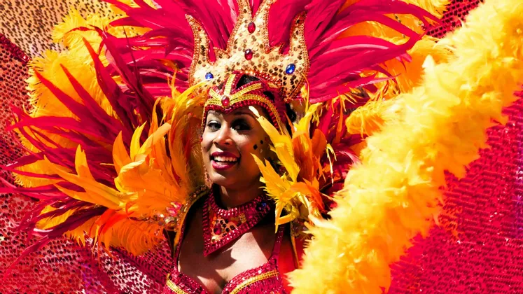 Eine lächelnde Frau mit farbenprächtigem rot-gelbem Federkopfschmuck und Paillettenkostüm für Karneval.
