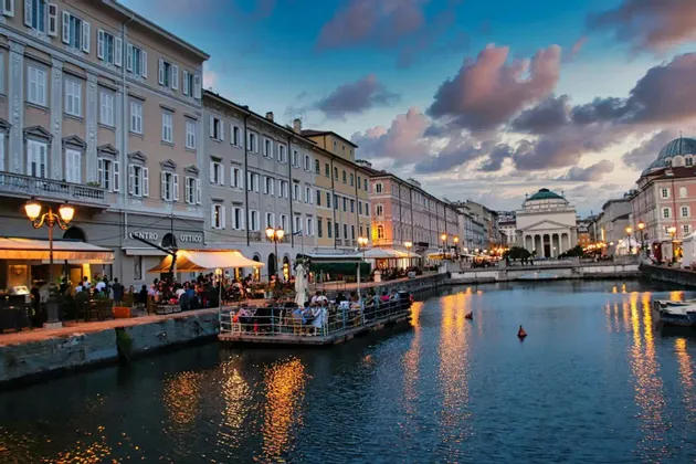 Un canale cittadino al tramonto, con persone che cenano nei ristoranti sul lungomare e luci che si riflettono sull'acqua.