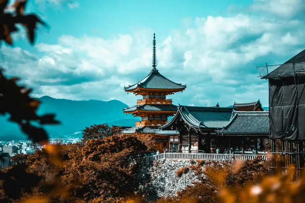 Una tradizionale pagoda a più livelli sorge su una collina che domina una città e le montagne sotto un cielo nuvoloso.