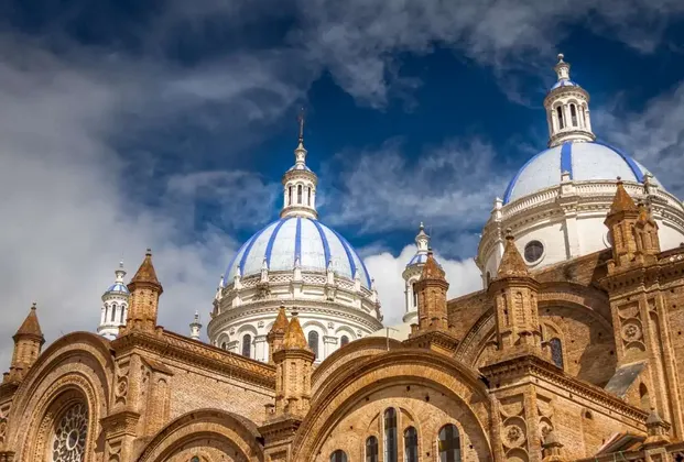 Una vista dal basso di una cattedrale in mattoni ornata con grandi cupole a strisce blu e bianche contro un cielo nuvoloso.