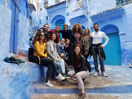 Un voyage de groupe WeRoad posant pour une photo sur les marches d'une ruelle étroite aux murs bleus distinctifs.