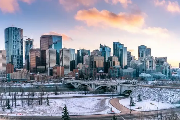 Uno skyline cittadino con alti edifici in vetro domina un fiume e un ponte, con terreno coperto di neve in primo piano.