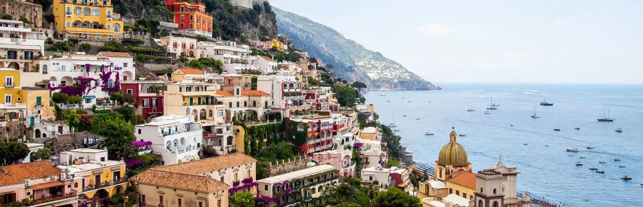 Vista panorámica de edificios coloridos en un acantilado empinado, con un mar azul salpicado de barcos bajo un cielo claro.