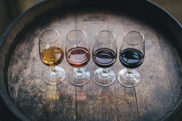 Quattro calici di vino con una sfumatura di colore da chiaro a scuro, disposti per una degustazione su una botte di legno.
