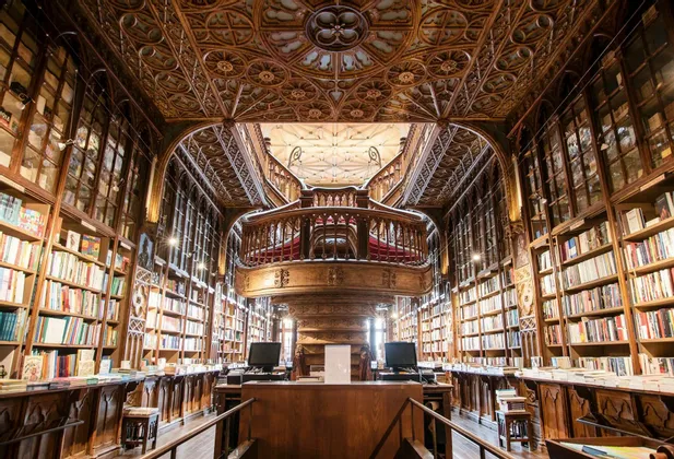 L'interno di una sfarzosa biblioteca in legno a più piani con una grande scalinata centrale e scaffali a tutta altezza.