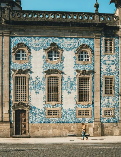 Una persona cammina su un marciapiede davanti a una facciata di un edificio coperta di intricate piastrelle decorative blu e bianche.