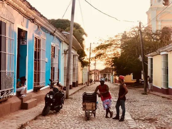 Due uomini parlano su una strada acciottolata fiancheggiata da case coloniali colorate al tramonto.