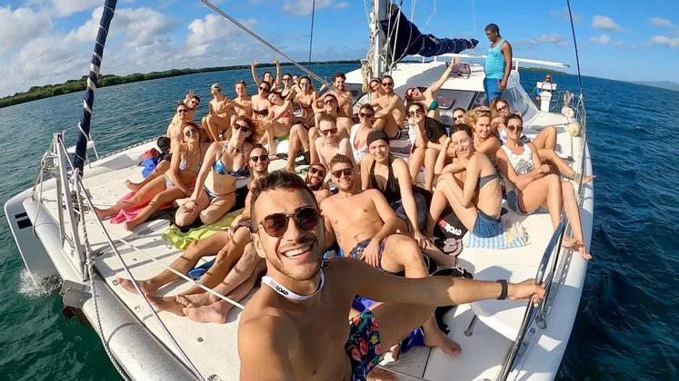 Un numeroso gruppo WeRoad sorride e posa per un selfie sul ponte di un catamarano che naviga in mare aperto.