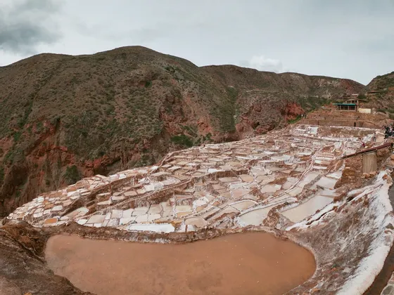 Salinas en terrazas, blancas y marrones, en la ladera de una montaña bajo un cielo cubierto.