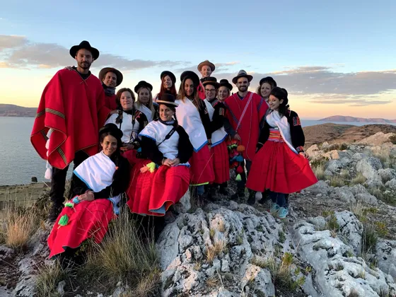 Un viaje en grupo de WeRoad con ropa tradicional roja y blanca posa en una colina rocosa con vistas a un cuerpo de agua al atardecer.
