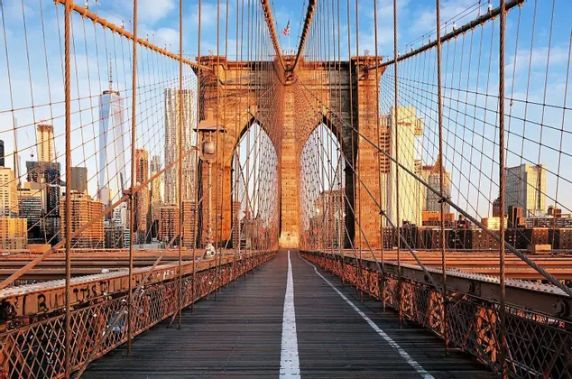 Une passerelle en bois vide sur un pont suspendu avec des arches en pierre menant vers une ligne d'horizon urbaine au lever du soleil.