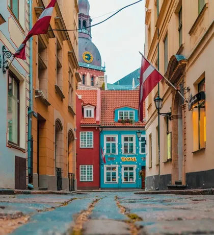 A low-angle shot of a narrow cobblestone street flanked by colorful buildings, with a clock tower visible in the background.