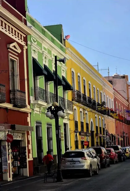 Una strada stretta con auto parcheggiate lungo una fila di edifici colorati, dipinti di rosso, verde e giallo.