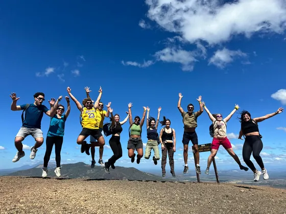 Un voyage en groupe WeRoad de onze personnes sautant à l'unisson au sommet d'une montagne sous un ciel bleu vif parsemé de nuages.