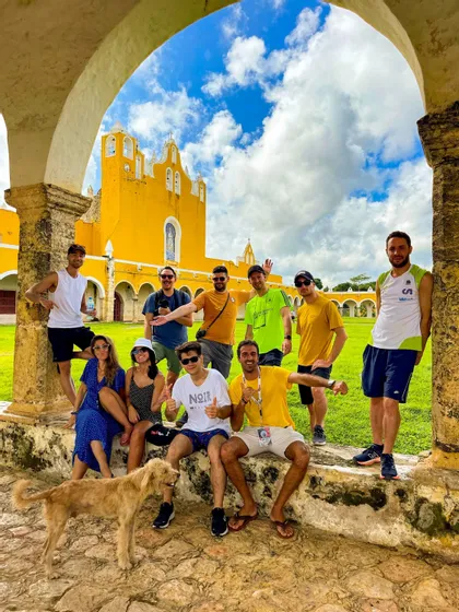 Un viaje en grupo de WeRoad posando para una foto bajo un arco de piedra, con un gran edificio amarillo de fondo y un perro cerca.