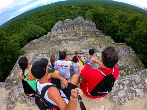 Un groupe WeRoad prend un selfie assis au sommet d'anciennes ruines de pierre, surplombant une vaste jungle verdoyante.