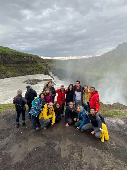 Un viaje en grupo de WeRoad posando para una foto en un mirador con vistas a una enorme cascada que cae en un cañón de río.