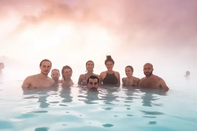 Un viaggio di gruppo WeRoad con persone sorridenti e rilassate nell'acqua azzurra, lattiginosa e fumante di una piscina termale.