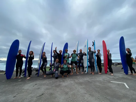 Un viaggio di gruppo WeRoad con persone in mute che posano con le loro tavole da surf su una passeggiata in riva all'oceano sotto un cielo nuvoloso.