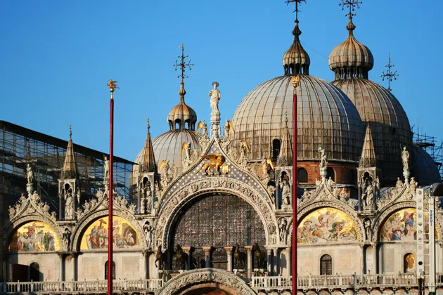La façade supérieure ornée d'une basilique, avec de grandes coupoles, des mosaïques dorées et des sculptures détaillées, sous un ciel bleu clair.