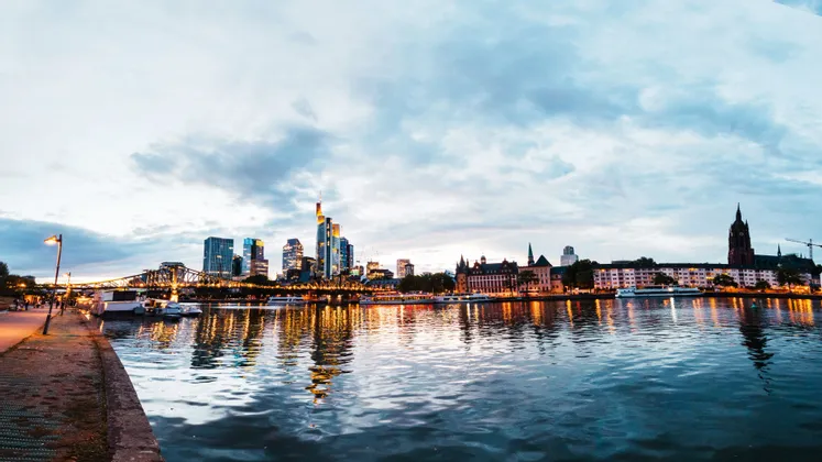 Uno skyline cittadino illuminato con grattacieli e un ponte che si riflettono sul fiume al tramonto.