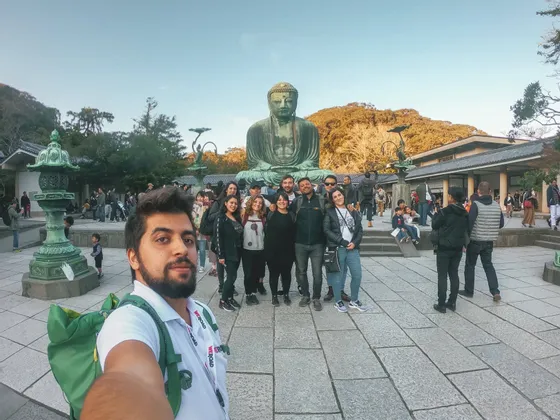 Ein Mann macht ein Selfie mit einer WeRoad-Reisegruppe, die in einem Innenhof vor einer großen bronzenen Buddha-Statue posiert.