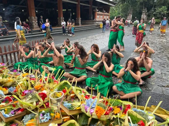 Un groupe WeRoad en tenue de cérémonie verte est assis au sol, priant devant des offrandes florales colorées.