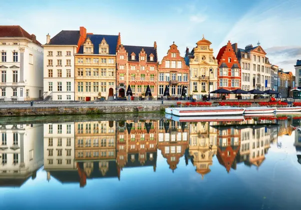 Coloridos edificios históricos con tejados a dos aguas bordean un canal, sus fachadas se reflejan en las tranquilas aguas.
