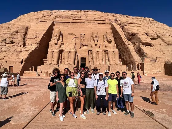 Un groupe WeRoad en voyage, posant pour une photo devant un grand temple taillé dans la roche, orné de quatre statues colossales assises.