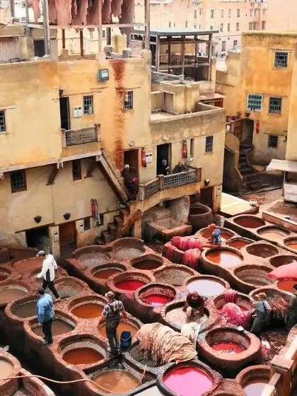 Hommes travaillant dans une tannerie traditionnelle en plein air, entourés de grandes cuves circulaires en pierre remplies de teintures colorées.