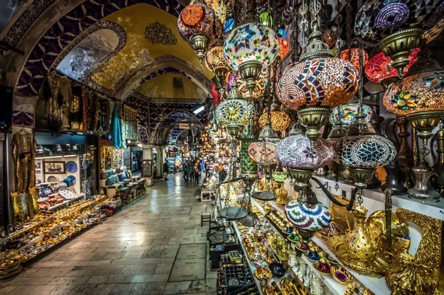 Bunte Mosaiklampen hängen auf einem belebten Innenmarkt mit gewölbten Decken und Ständen voller Waren zum Verkauf.