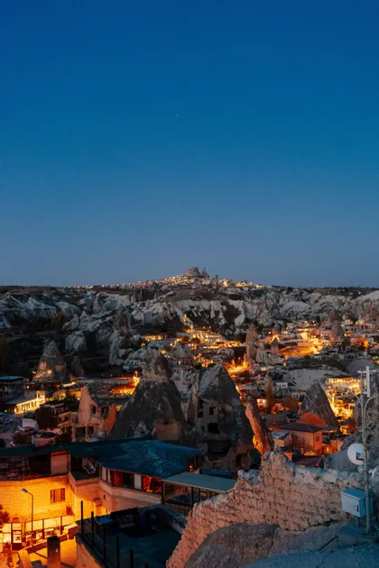 Une ville nichée parmi des formations rocheuses uniques, illuminée par les lumières au crépuscule sous un ciel bleu clair.