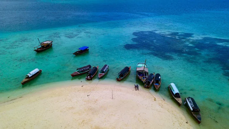 Una vista aérea de barcos de madera amarrados en un banco de arena, rodeados de aguas tropicales turquesas y azul profundo.