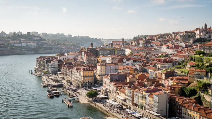 Veduta dall'alto di una città con edifici colorati e tetti in terracotta, costruita su un fianco di collina accanto a un ampio fiume.