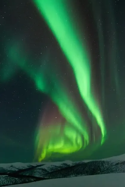Luces vibrantes de la aurora boreal verde giran en el cielo estrellado sobre un paisaje montañoso cubierto de nieve.